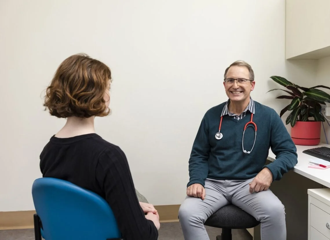 A doctor with a stethoscope talking to a female patient in a medical office.