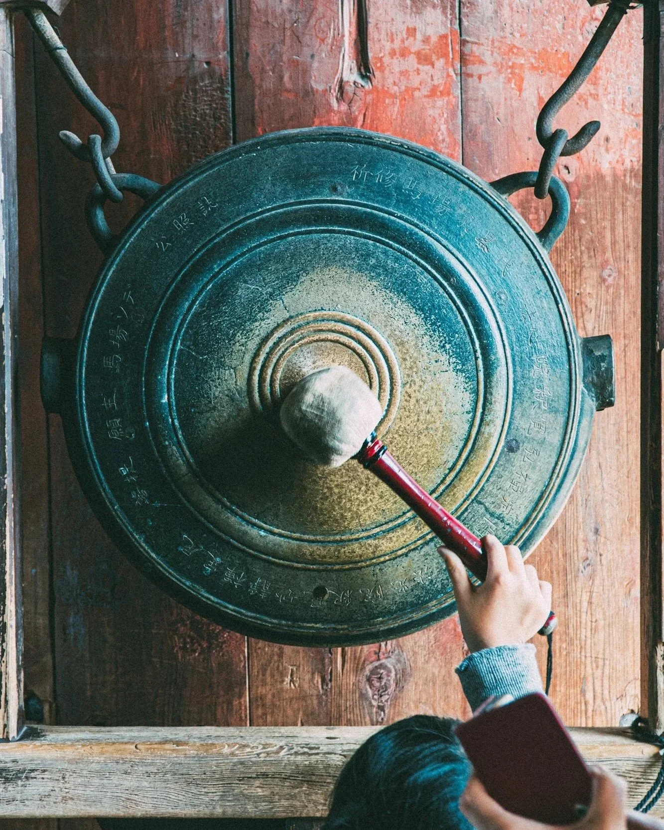 Person striking a large gong with a padded mallet during a sound session.