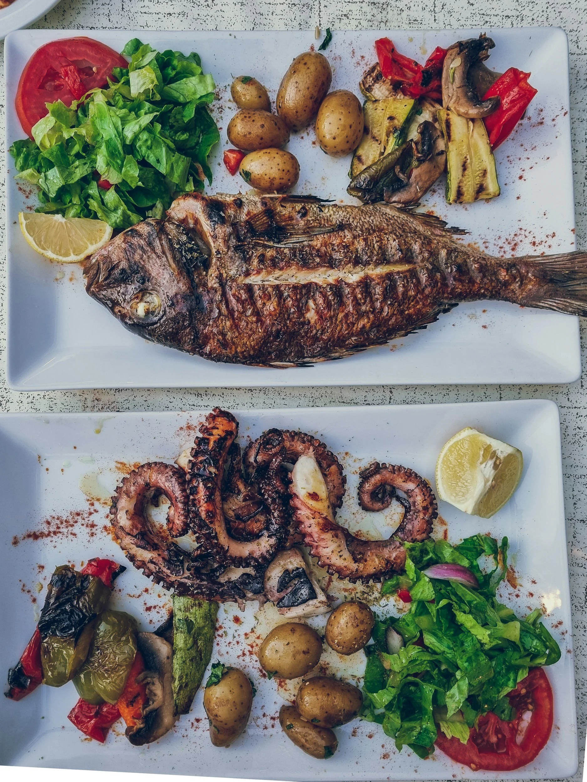 Grilled whole fish served with potatoes, vegetables, salad and lemon.