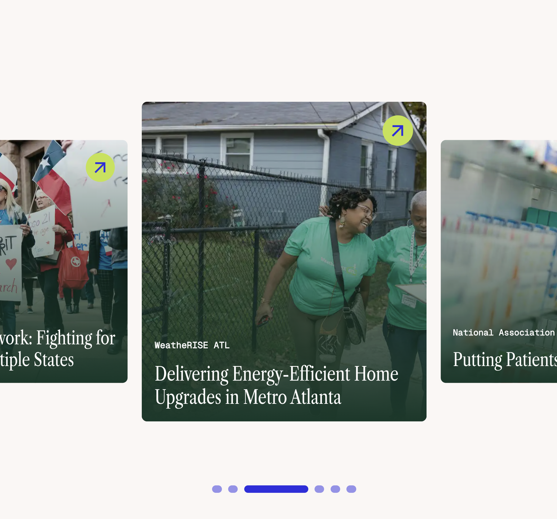 A woman wearing glasses and a green shirt, smiling, walks with another person in a green shirt outdoors near a fence.
