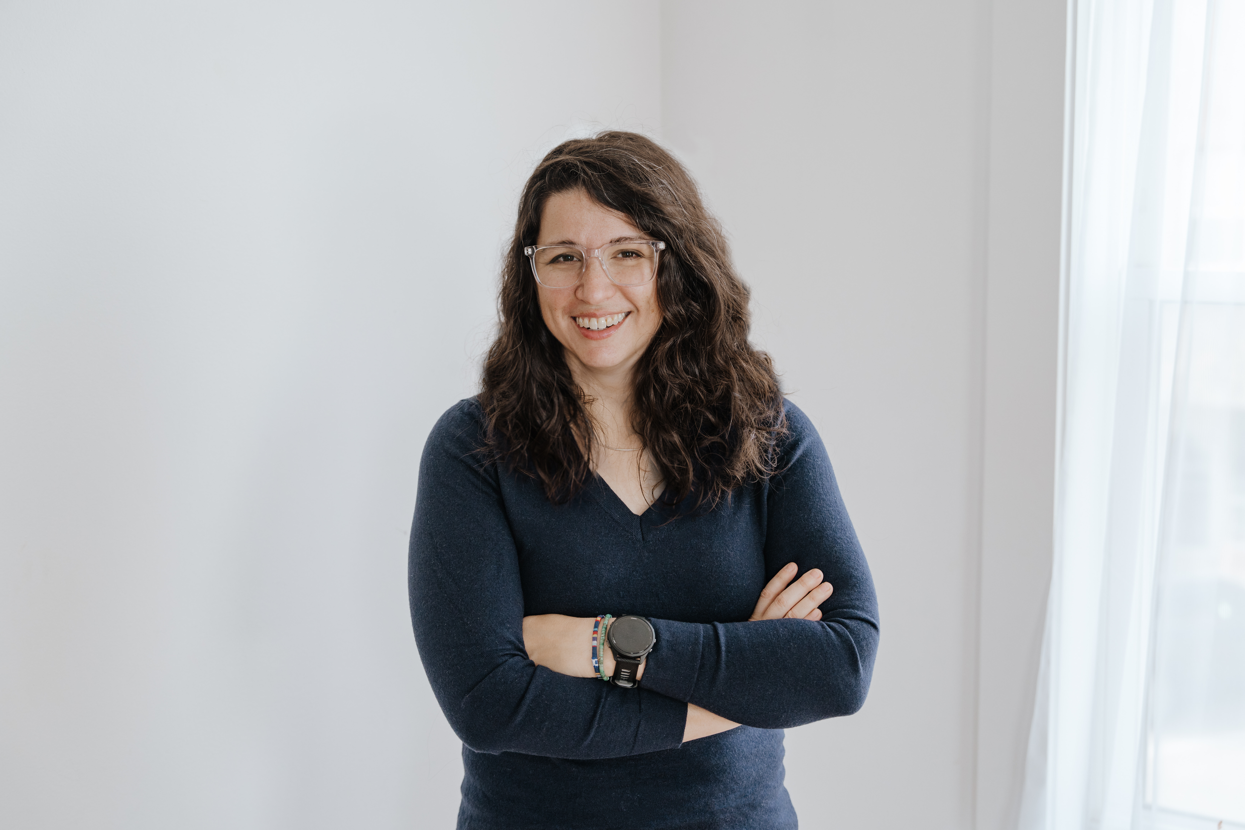 Cassie Tangney headshot - white background, woman in navy sweater, clear glasses and long brown hair.