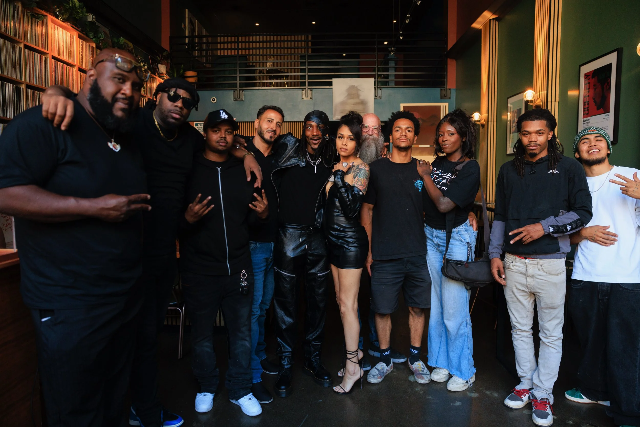 Group of ten diverse people standing together indoors, posing for a photo, with books and artwork on the walls around them.