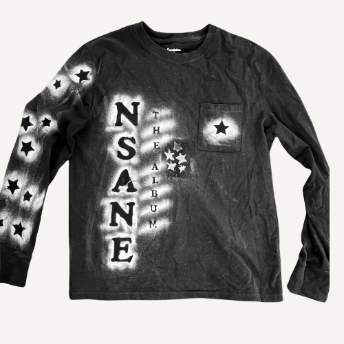 Black long sleeve shirt with stars and text reading 'NSA NONE THE ALBUM' on the front and stars on the sleeve and pocket.