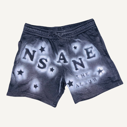 Black shorts with white paint splatter design and the word 'INSANE' spelled out across the front, with stars and 'The Album' printed below.