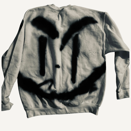 A sweatshirt with a black spray-painted smiley face that has large, arched eyebrows and a character-like expression.