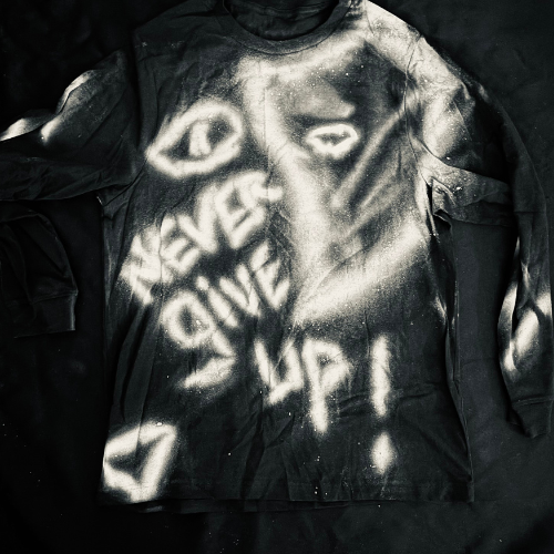 Black long-sleeve shirt with white spray-painted graffiti-style design and text reading "NEVER GIVE UP."