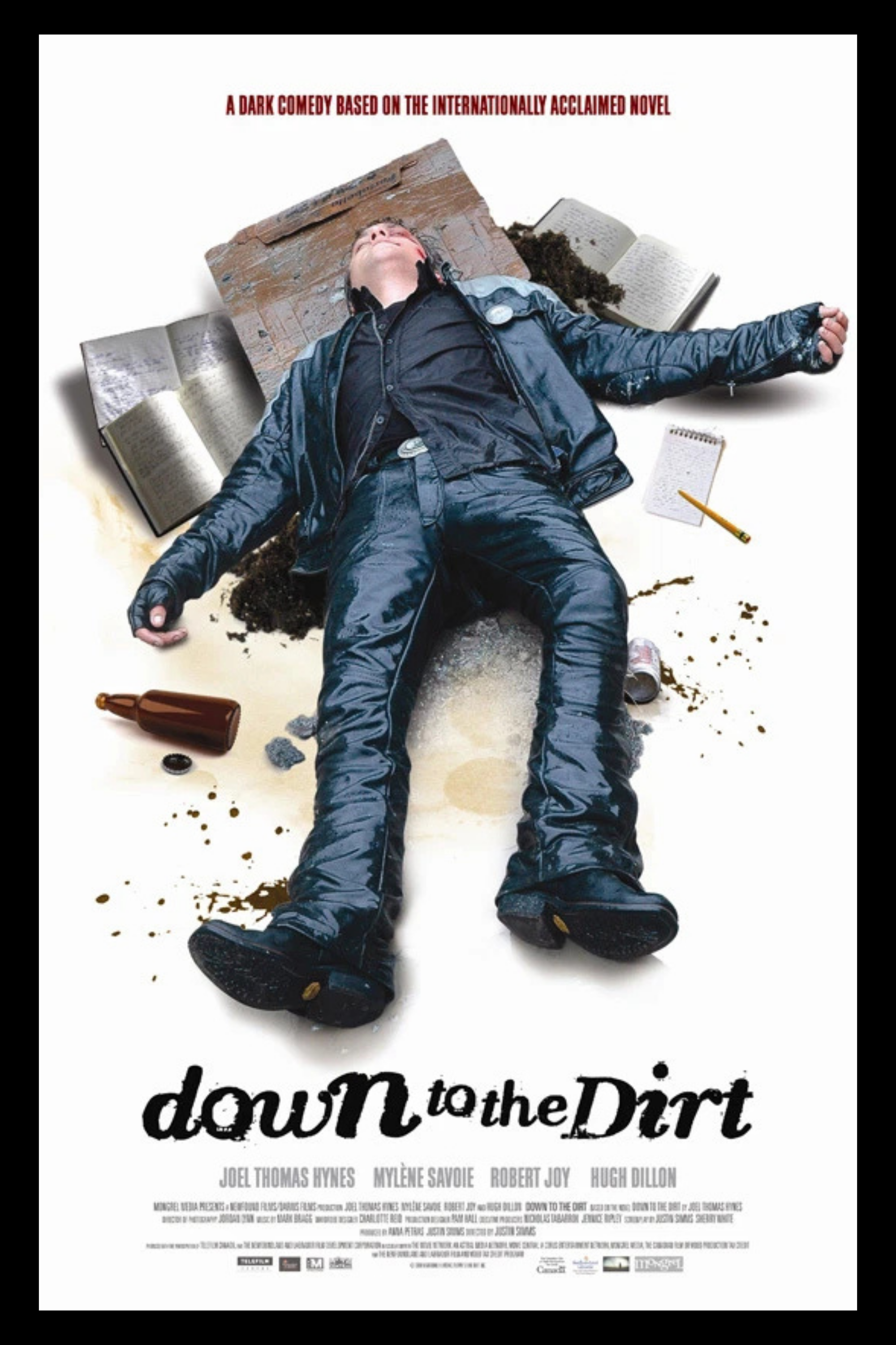 Person lying on the ground surrounded by books, a notebook, a bottle, and dirt, with the title "Down to the Dirt" and the tagline "A dark comedy based on the internationally acclaimed novel" above.