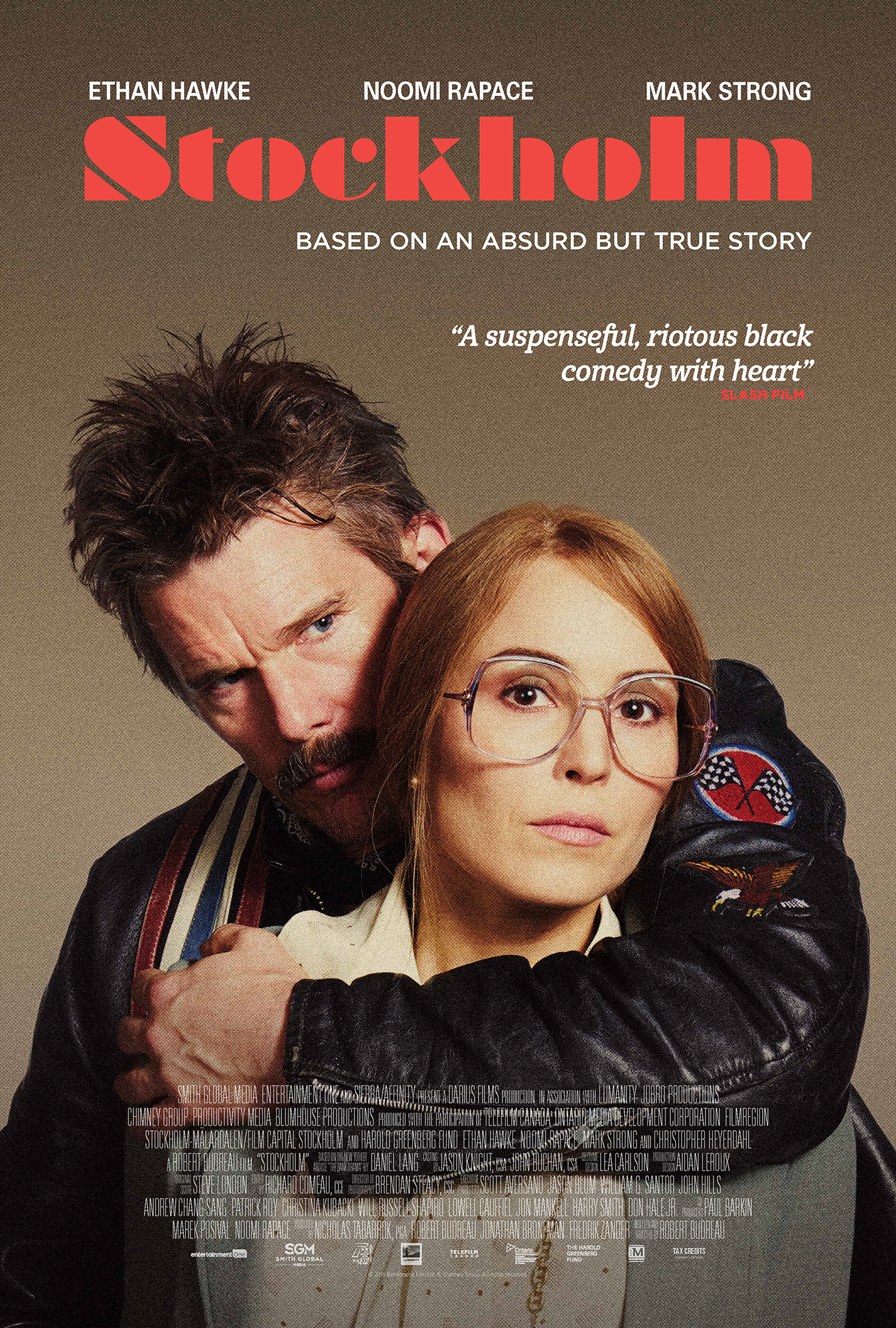 A movie poster for 'Stockholm' featuring Ethan Hawke and Noomi Rapace. Ethan Hawke is behind Noomi Rapace, hugging her and looking intensely at the camera. Noomi Rapace is wearing glasses and has a neutral expression. The background is gray, with the title in large red letters and various text elements.