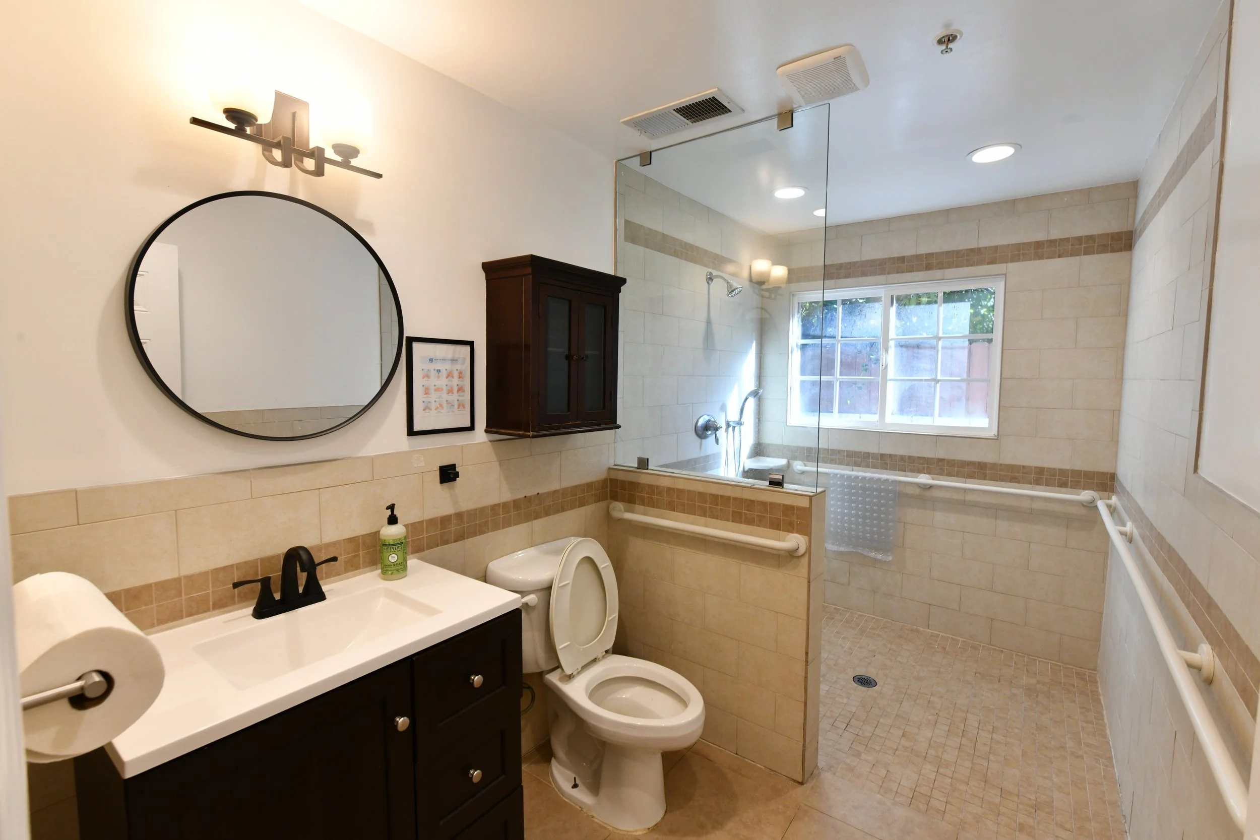 Bathroom with a vanity, mirror, toilet, and walk-in shower with glass partition and window.
