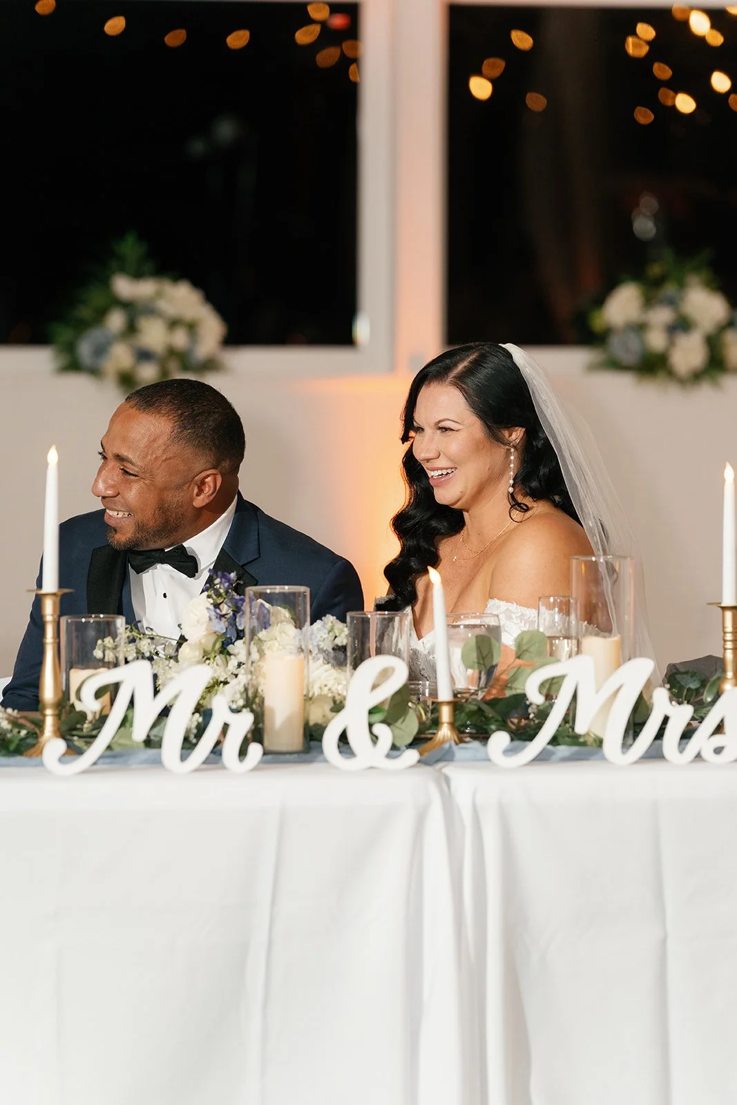 Happy bride and groom sitting at wedding reception table with candles and floral decorations.
