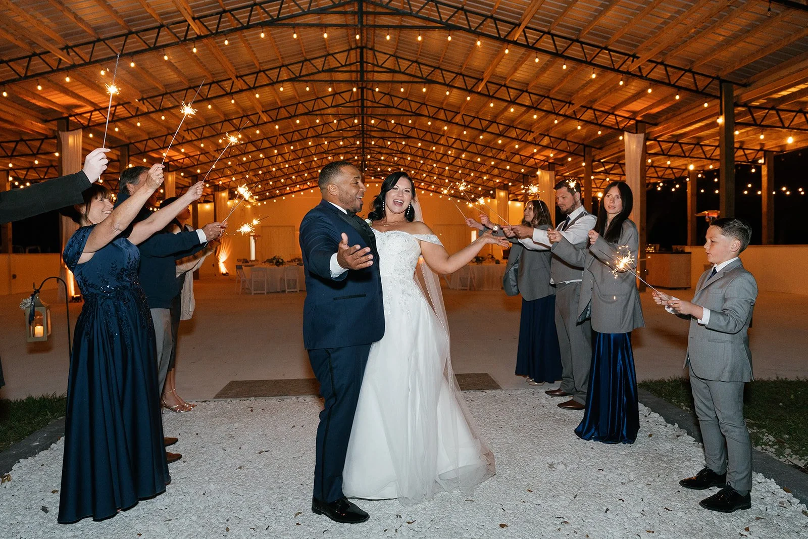Bride and groom dancing surrounded by guests holding sparklers at night in a decorated venue with string lights.