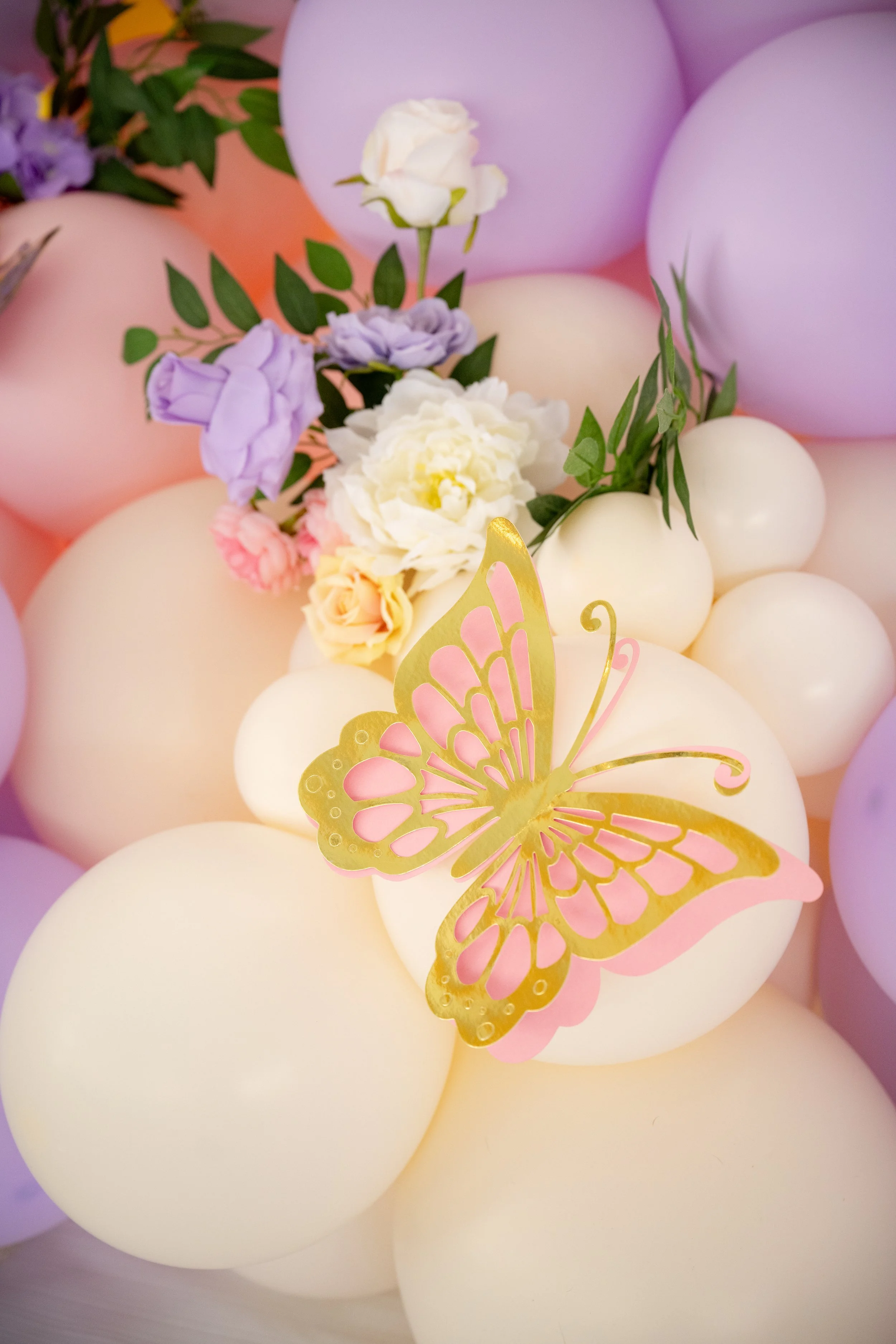 Purple, pink, and white balloons with floral decorations and gold butterfly cutout for a celebration or party.
