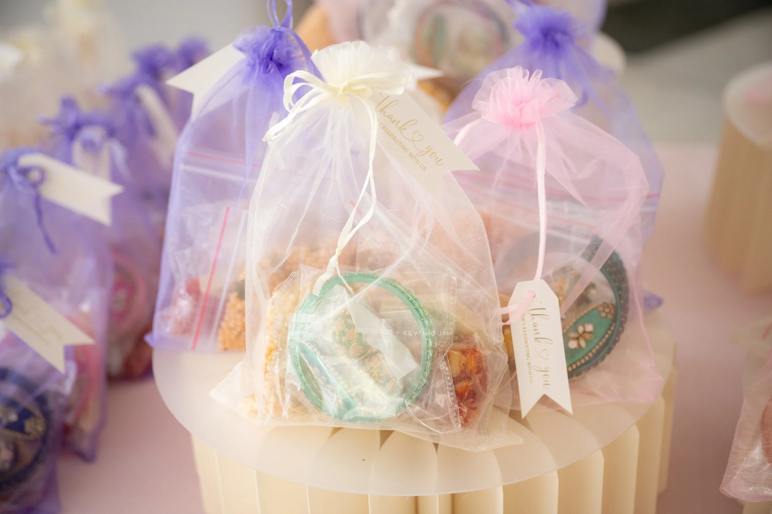 Small gift bags with tulle fabric and pastel-colored embellishments, labeled with tags saying 'thank you', arranged on a table.