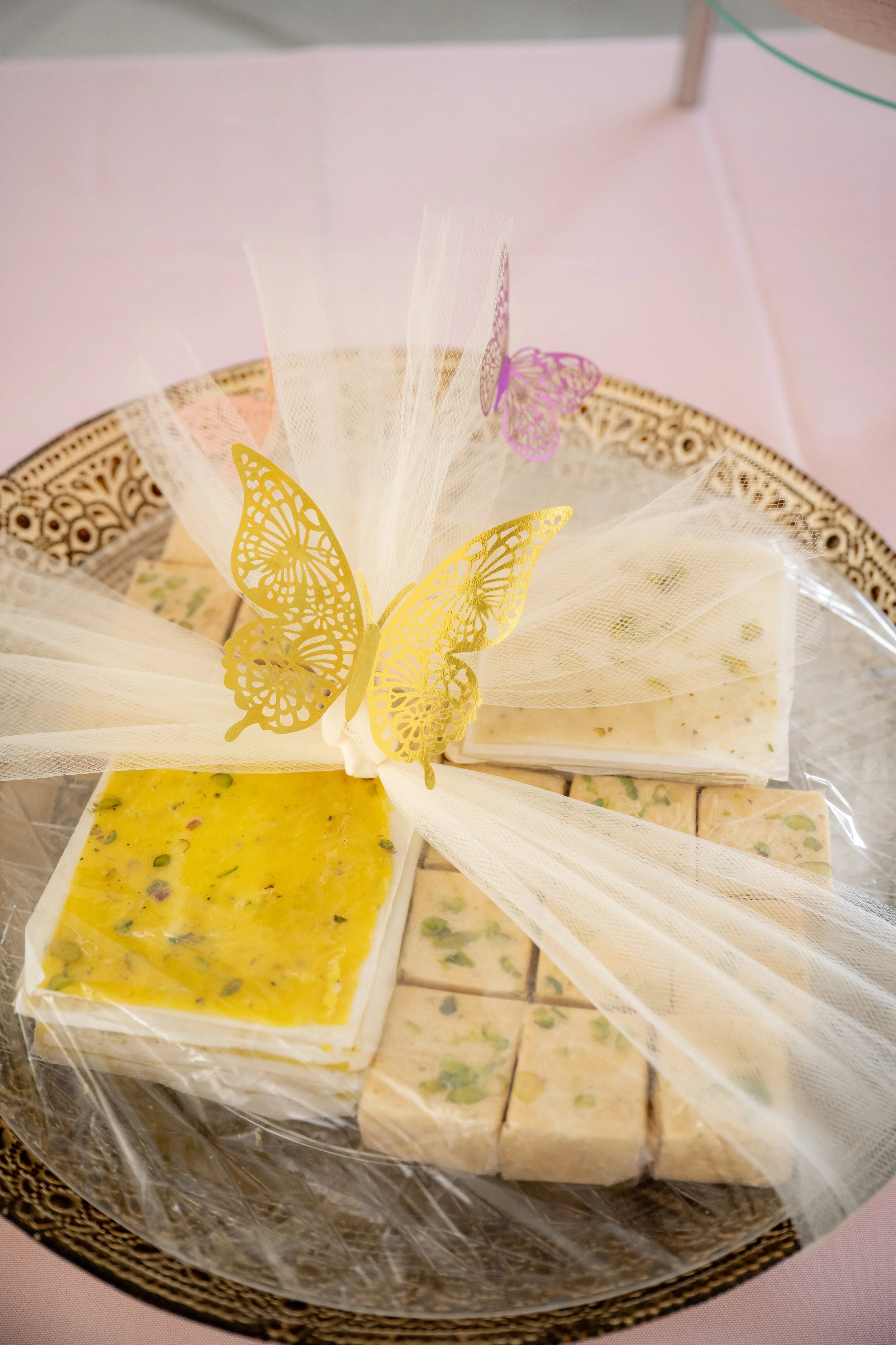 Assorted homemade soap bars with colorful toppings, wrapped in decorative butterfly and tulle wrapping, placed on a decorative tray.