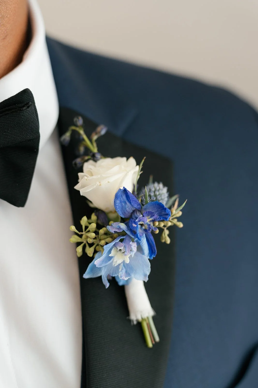 Close-up of a man's tuxedo with a boutonniere consisting of white and blue flowers on the lapel.