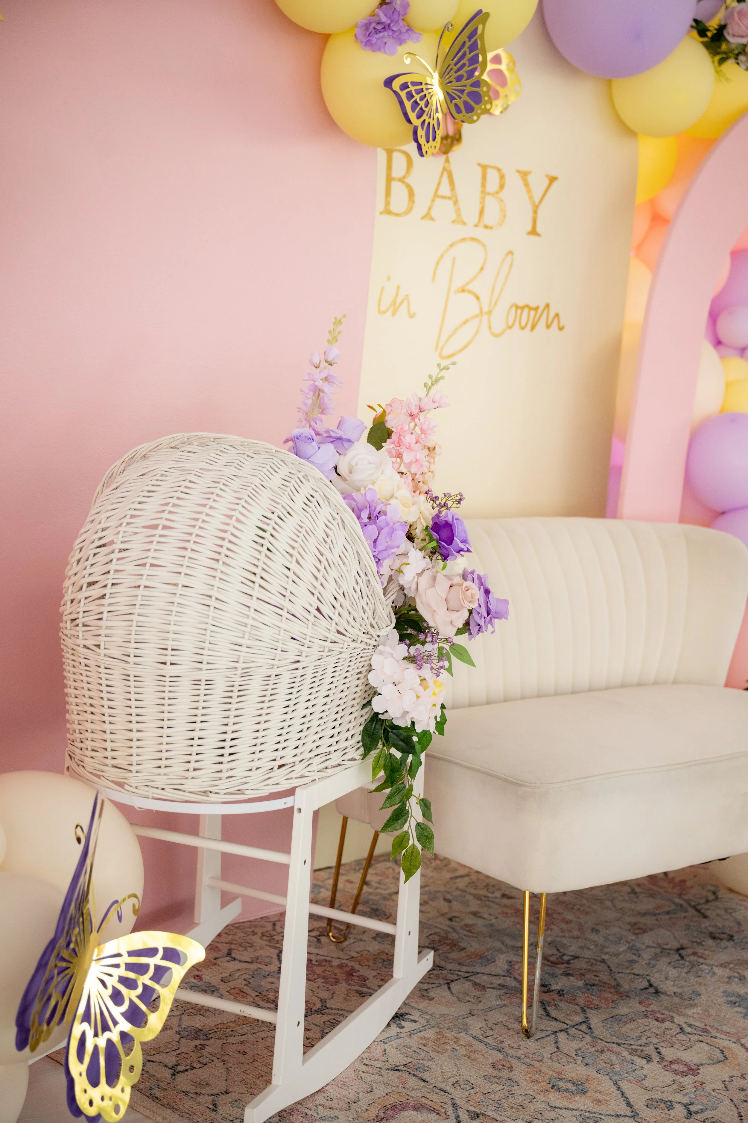 Decorative setup for a baby shower with pastel-colored balloons, a pink and purple theme, floral arrangements, and a sign that reads 'Baby in Bloom'.