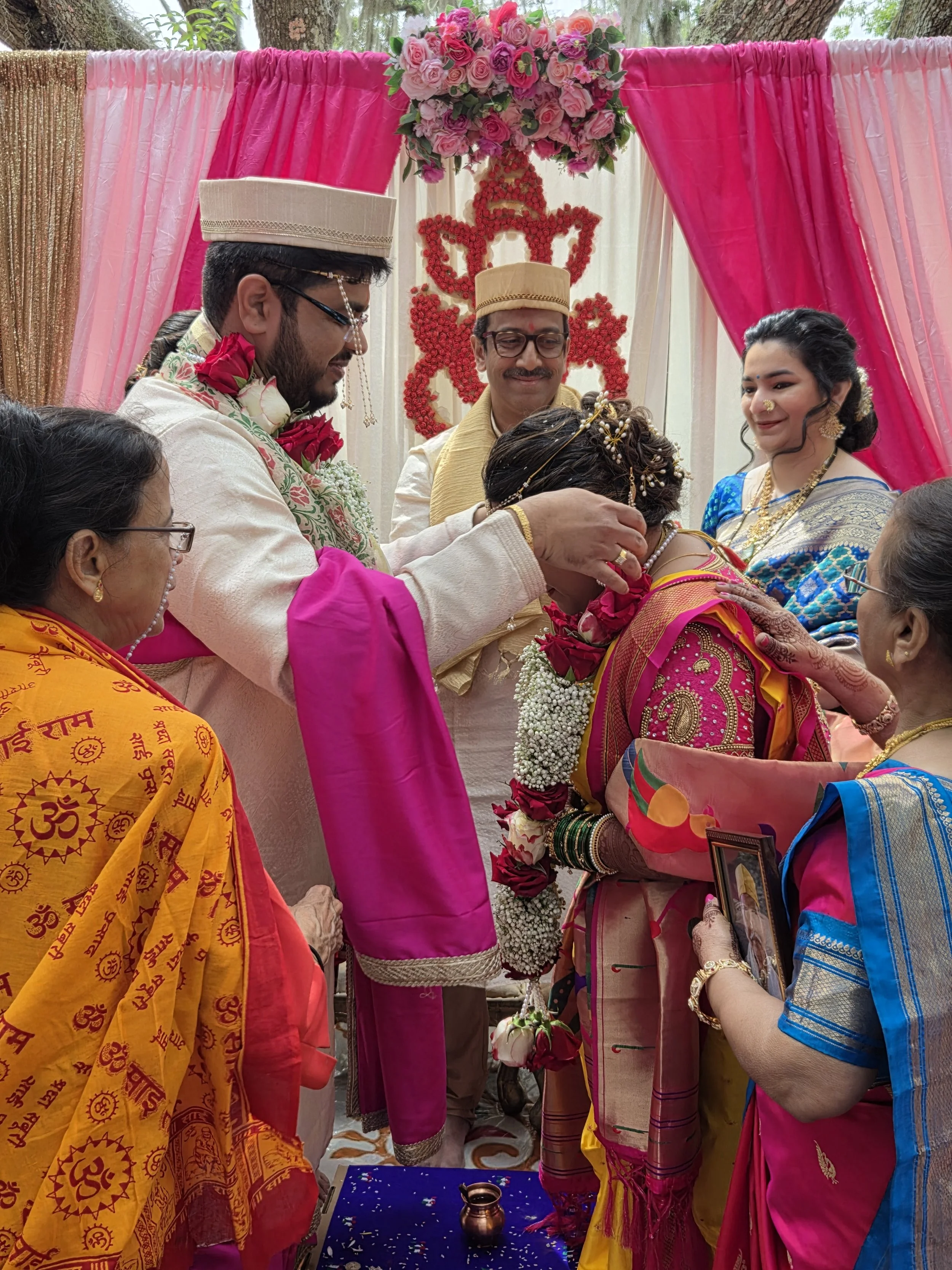 Hindu wedding ceremony with bride, groom, and family members in traditional attire, flowers, and colorful decorations.