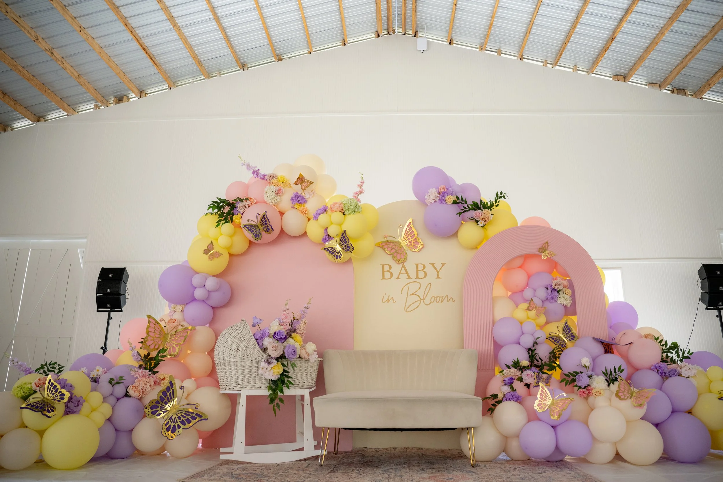 Decorative backdrop featuring pastel balloons, flowers, and golden butterfly accents for a baby shower with the words 'Baby in Bloom'