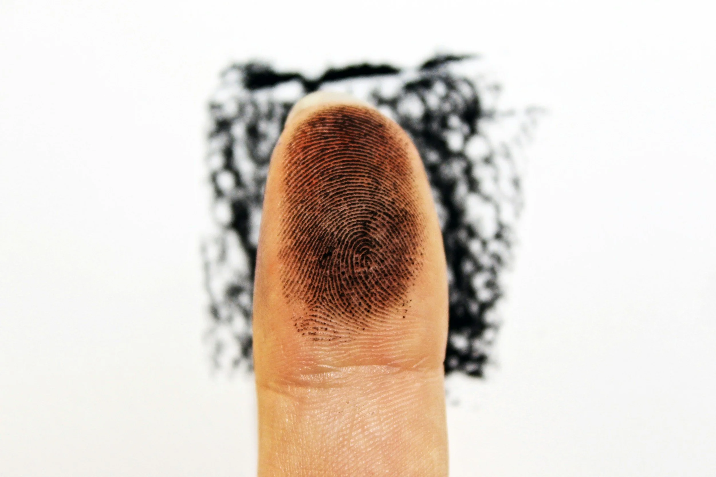 A close-up of a finger with a black fingerprint smudge on the tip, with a blurred black and white sponge in the background.