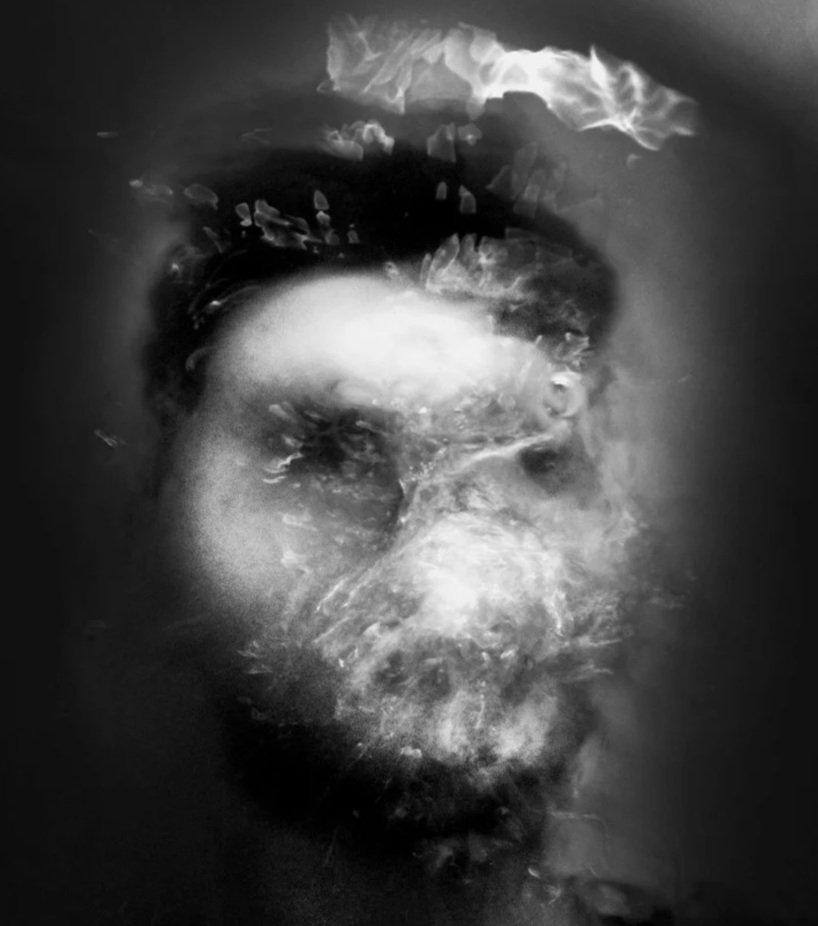Black and white photo of a woman's face underwater, partially obscured by bubbles and ripples.