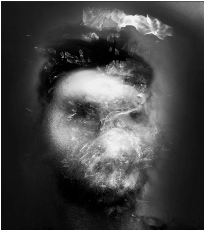 Black and white photo of a woman's face underwater, partially obscured by bubbles and ripples.