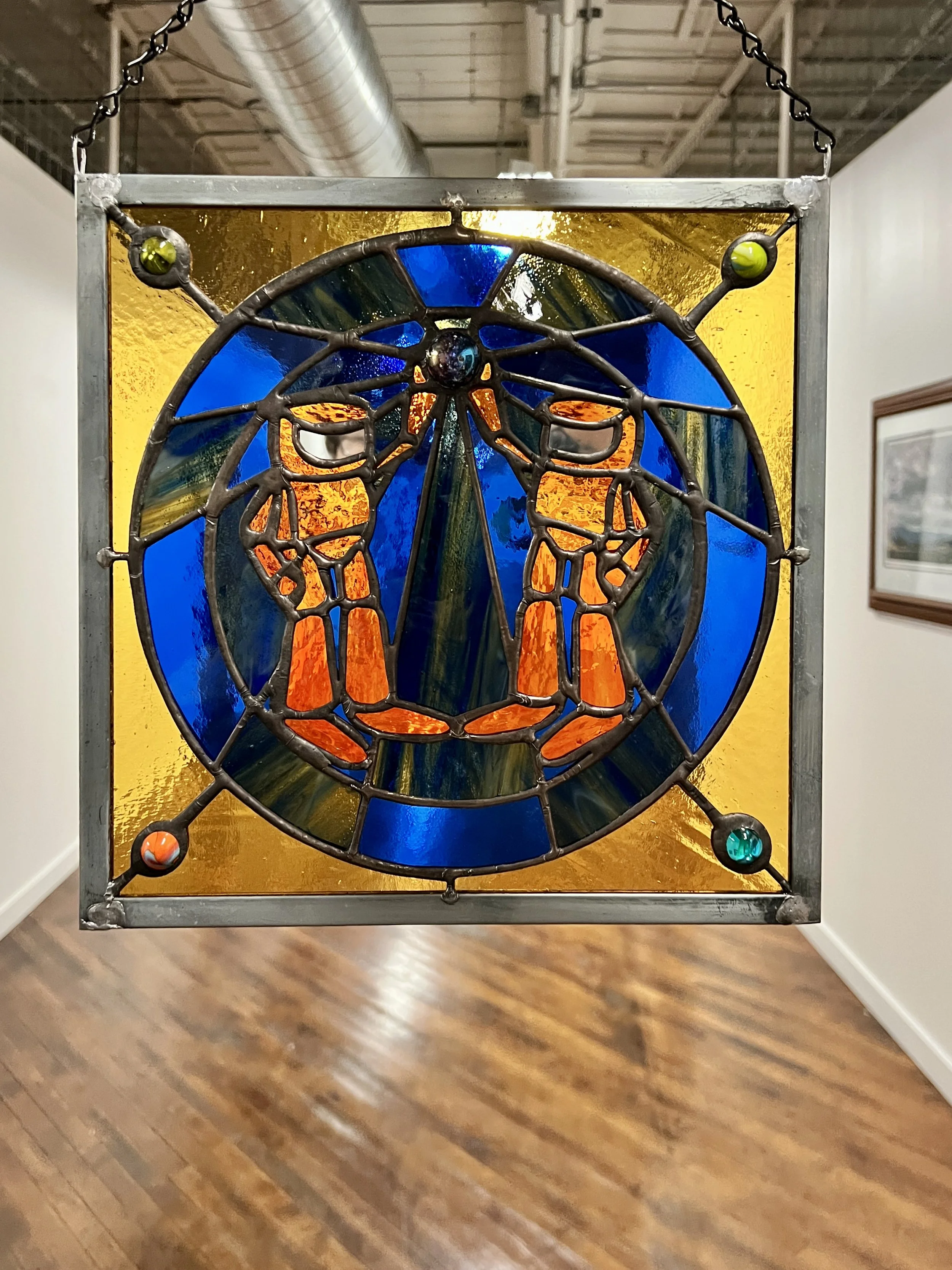 Stained glass artwork featuring a face with glasses and a nose, set against a yellow background.