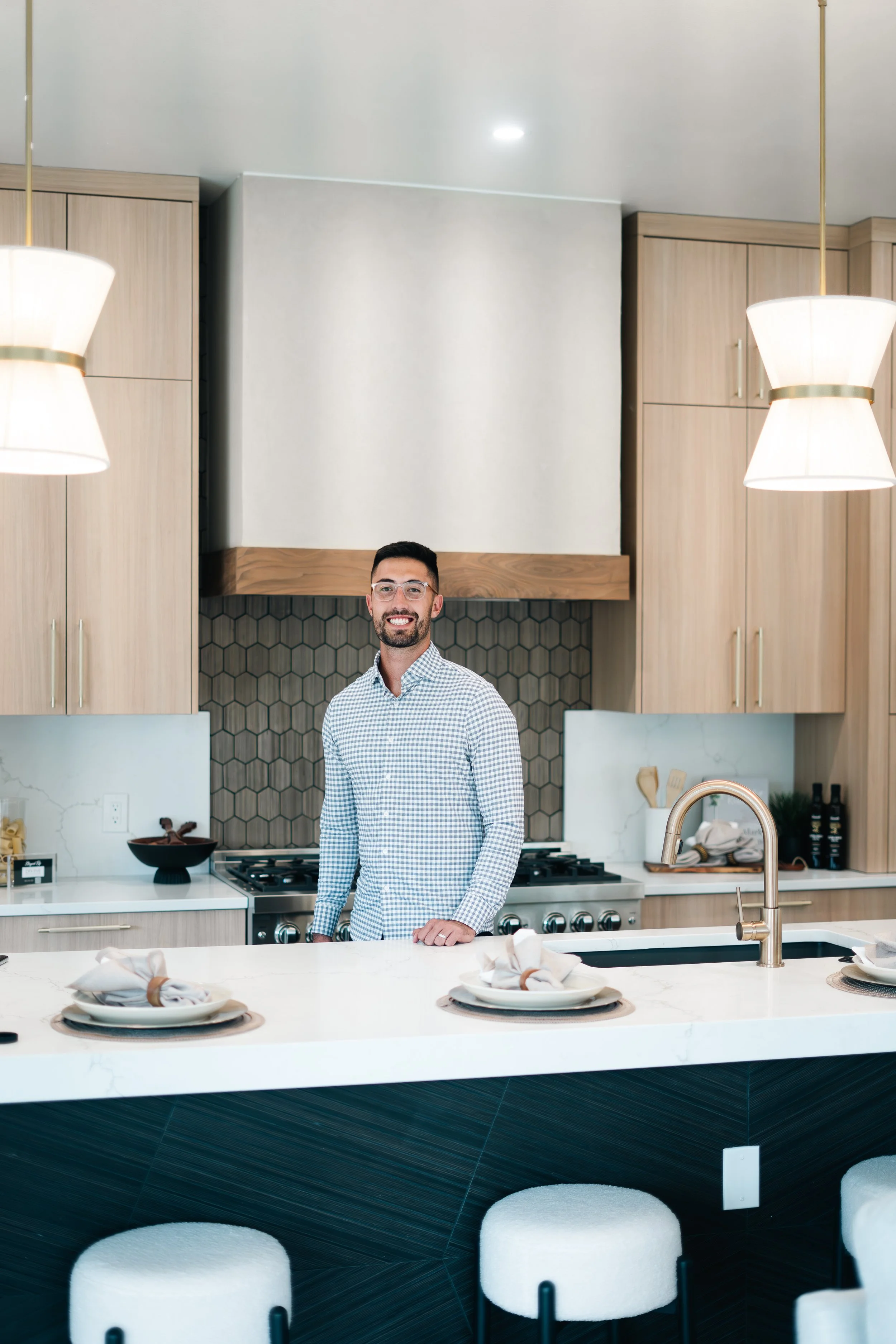 A man with glasses and a checkered shirt standing in a modern kitchen behind a white island.