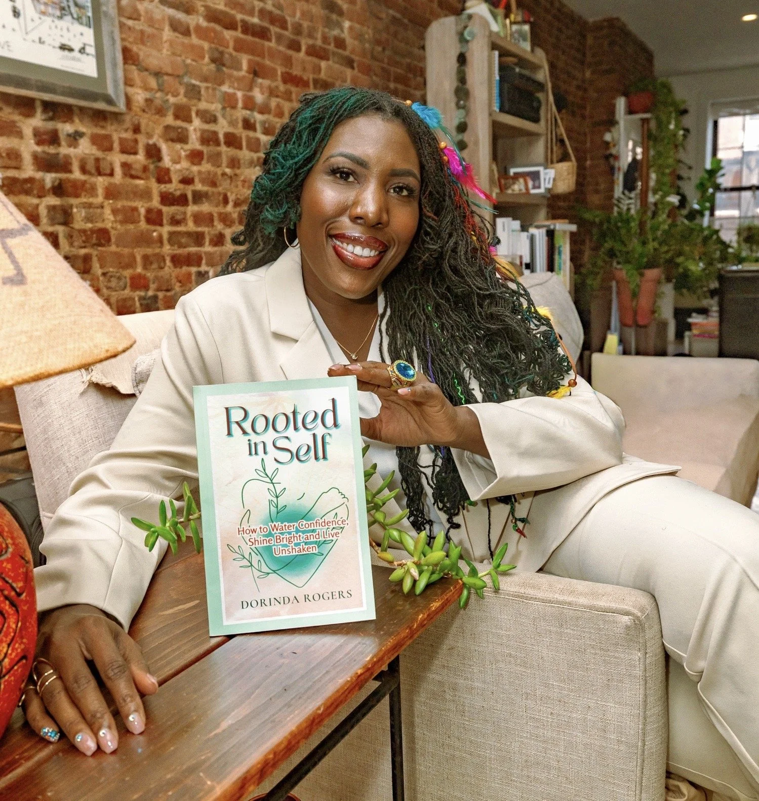 Rindy sitting in calm reflective space holding Rooted in Self book Helping women heal from the inside out