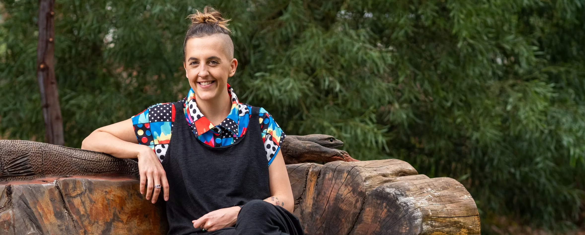 Zan Maeder, Adelaide based narrative therapist and doula sitting on a bench in a park and smiling.
