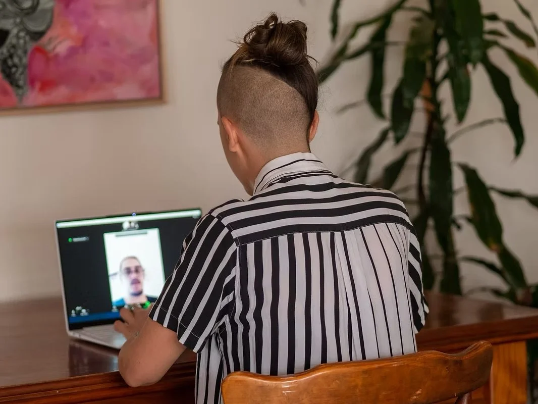 Zan sitting at their desk talking to a client on their laptop. View is of Zan's back. Zan is wearing a black and white striped shirt.
