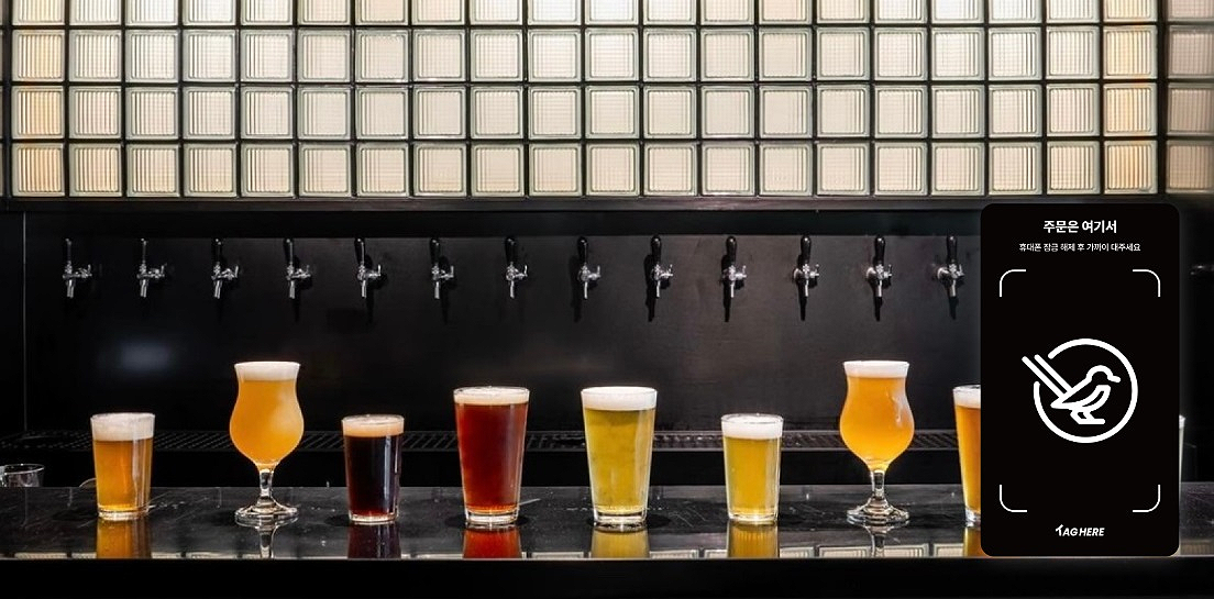 A row of various types of beers in different glasses on a bar counter with tap handles behind them.