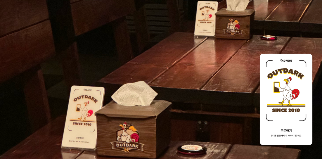 Wooden table with tissue box, promotional cards, and small wooden box, in a dimly lit setting.