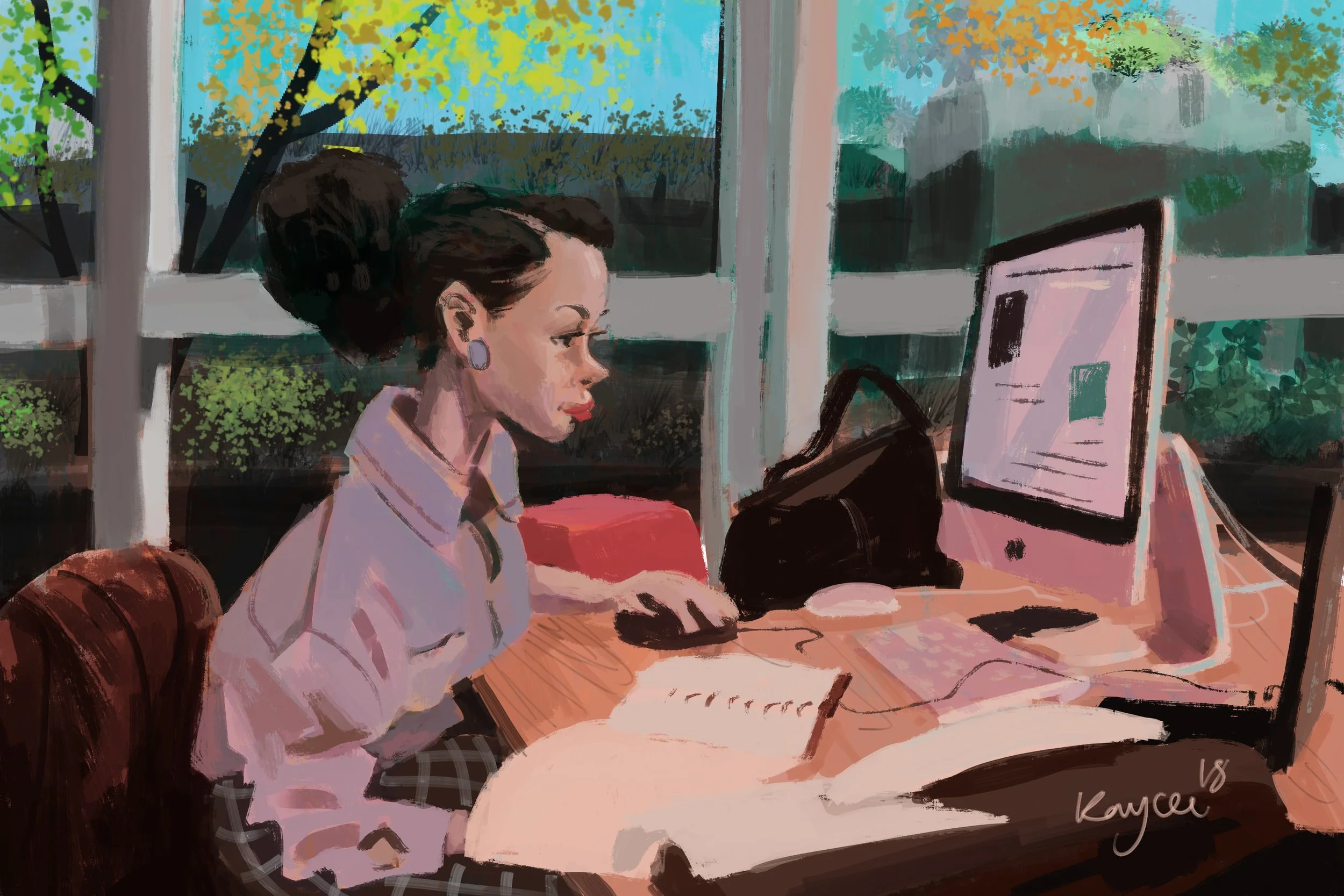 A woman with dark hair tied in a bun, wearing a light pink blouse and checkered pants, sitting at a desk, working on a computer, with a notebook and a bag nearby, with large windows showing trees outside.