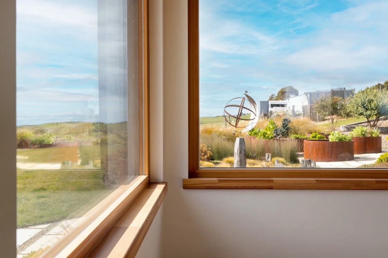 View of a landscaped yard with a sundial sculpture, greenery, and modern structures outside the window.
