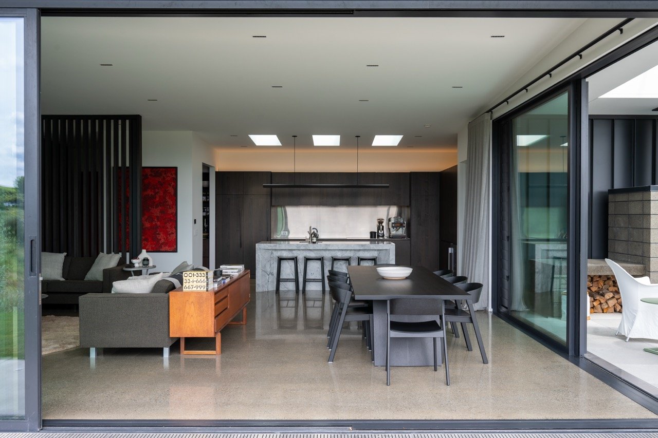 Modern open-concept living and dining area with a kitchen, stairs, and outdoor patio visible through large sliding glass doors.