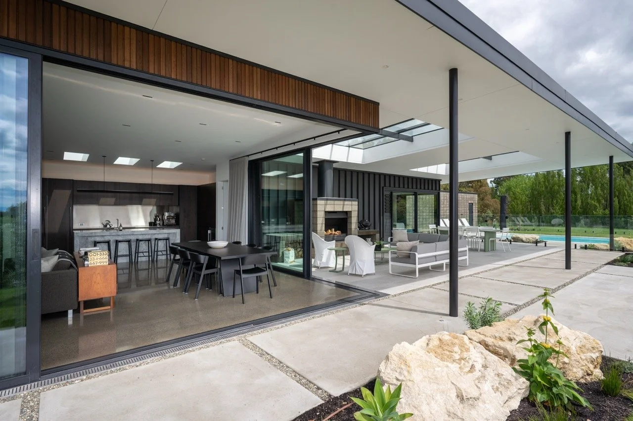 Modern house with an open-concept indoor and outdoor living space, featuring a kitchen, dining area, sitting area, and patio with outdoor furniture and a pool in the backyard.