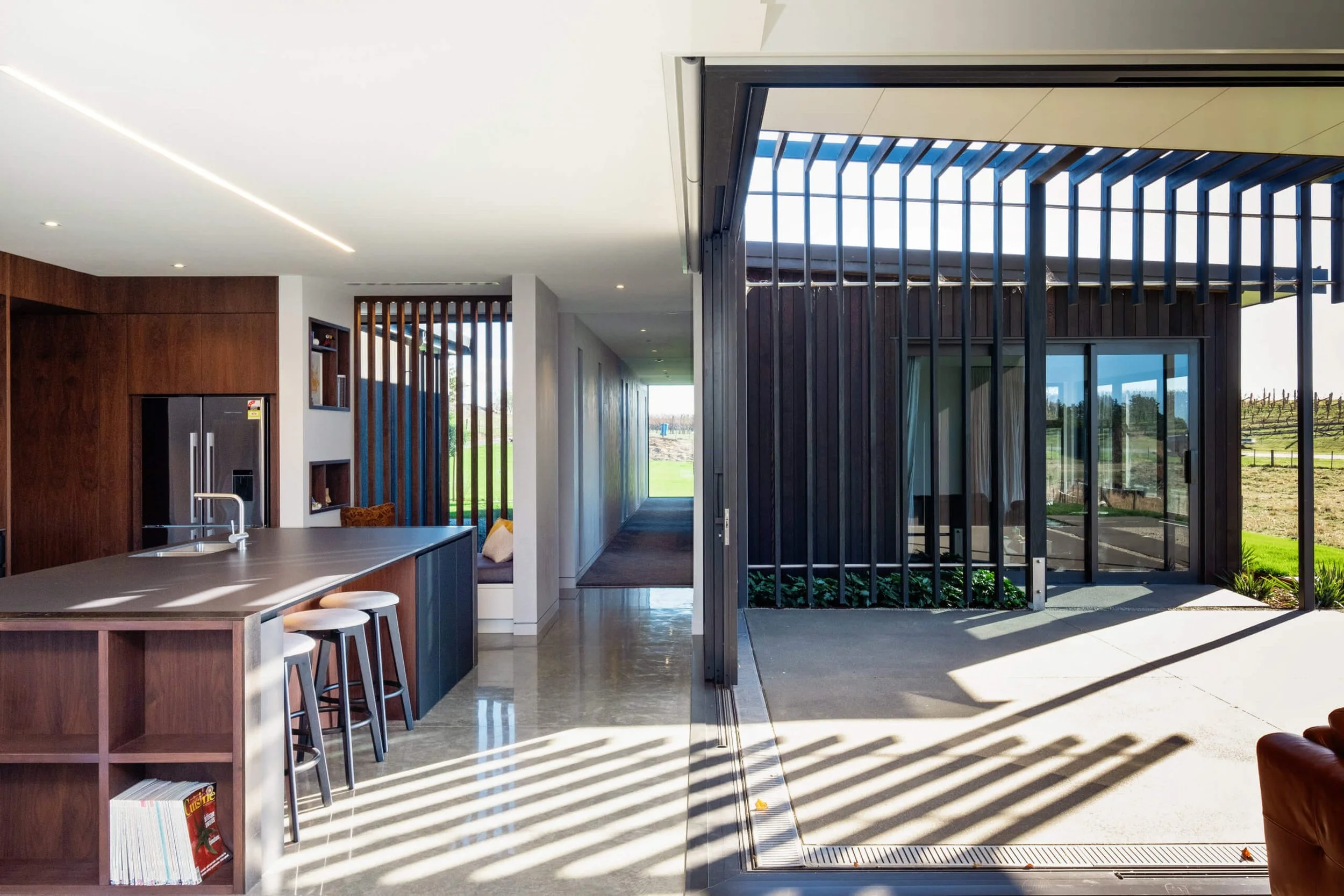 Modern open-concept kitchen and living space with large glass sliding doors revealing an outdoor patio and green landscape.