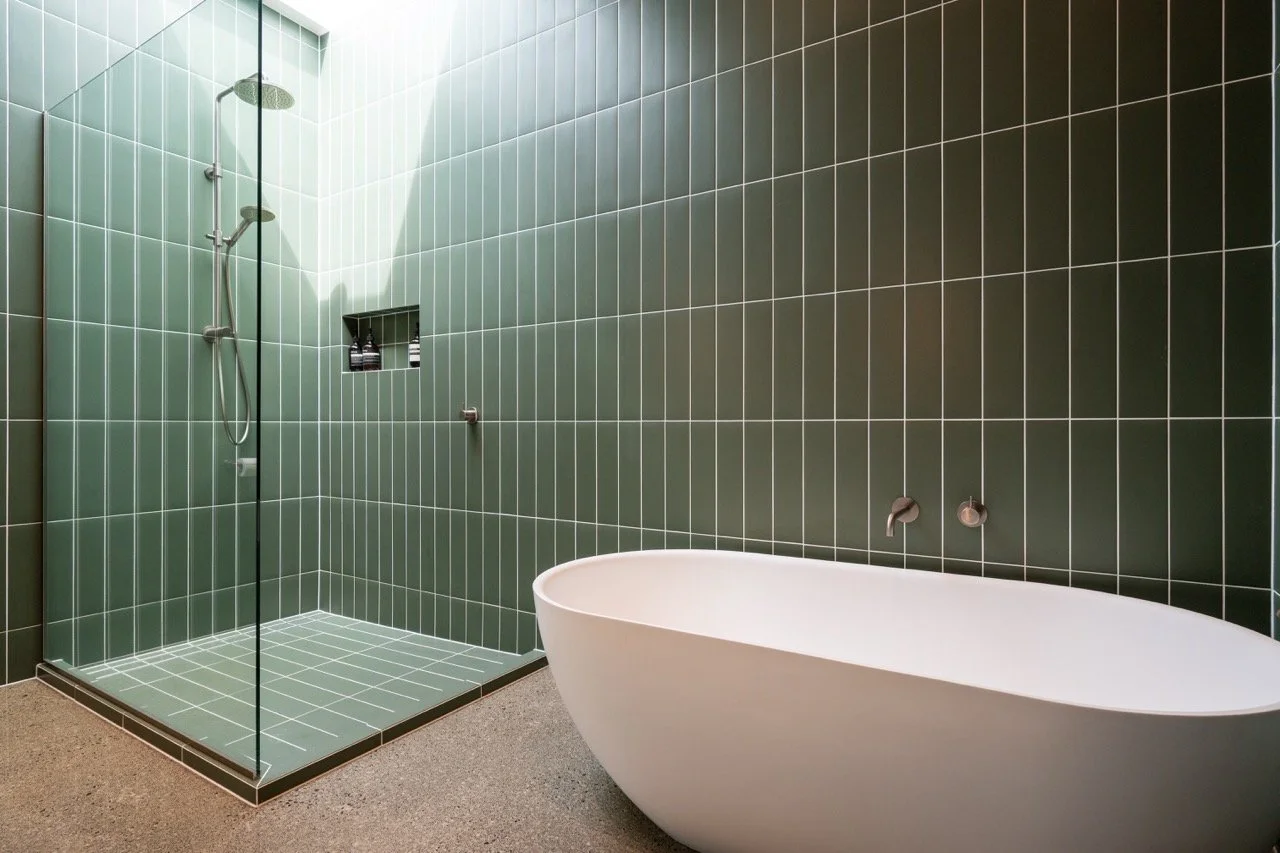 Modern bathroom with green tiled shower and freestanding bathtub.