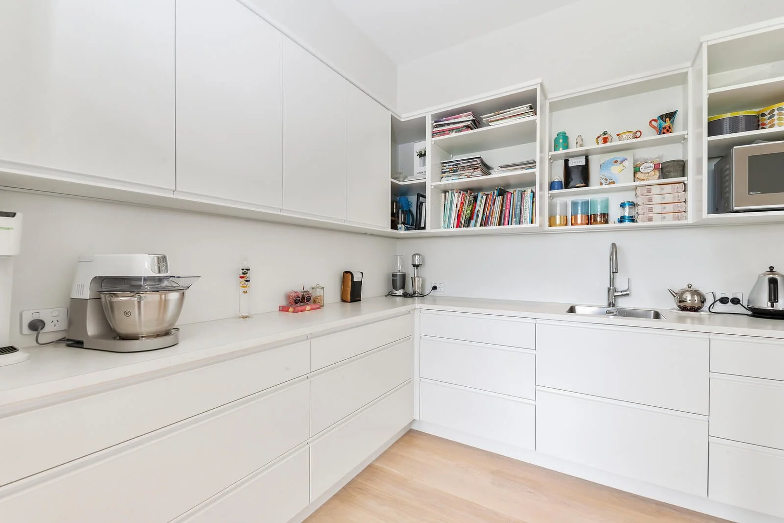 Modern white kitchen with open shelving, kitchen appliances, and light wooden flooring.