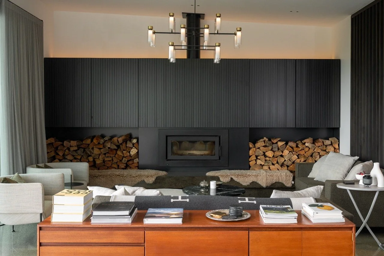 Modern living room with built-in black fireplace, stacked firewood, beige and gray seating, and minimalist decor.