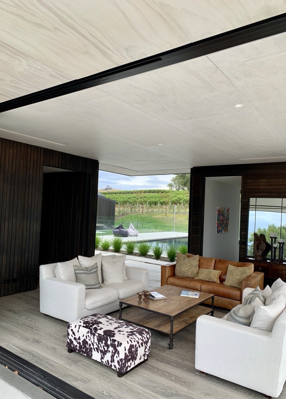 Living room with white and brown sofas, wooden coffee table, view of outdoor pool and vineyard through large window, modern decor.