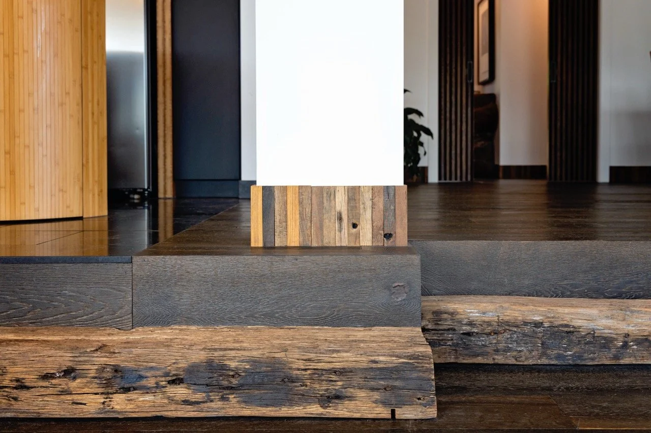 Close-up of a wooden staircase with a mix of dark and weathered wood, leading up to a modern interior with white walls and wooden accents.