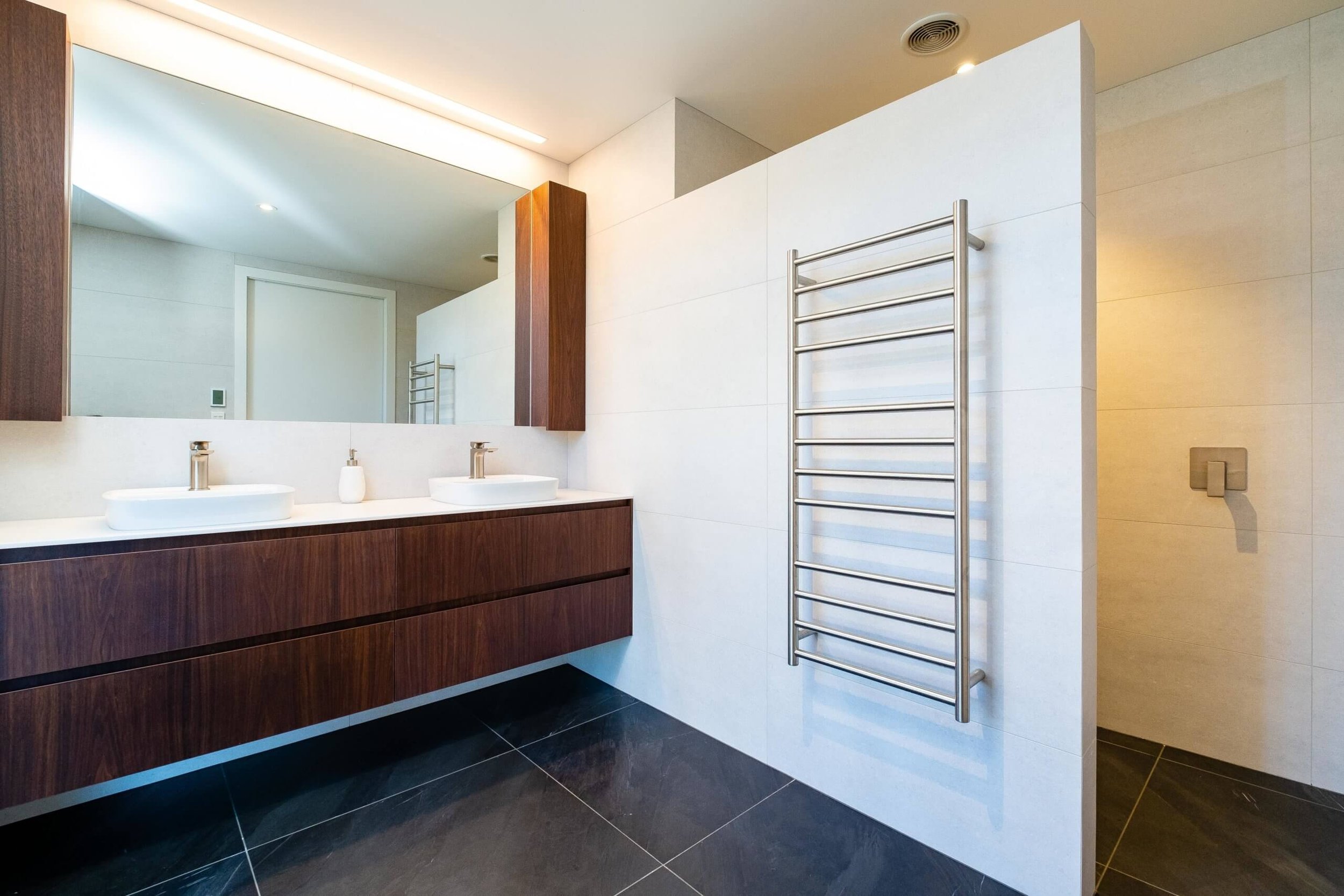 Modern bathroom with double vanity sinks, large mirror, wood cabinetry, and a heated towel rail on a white wall.