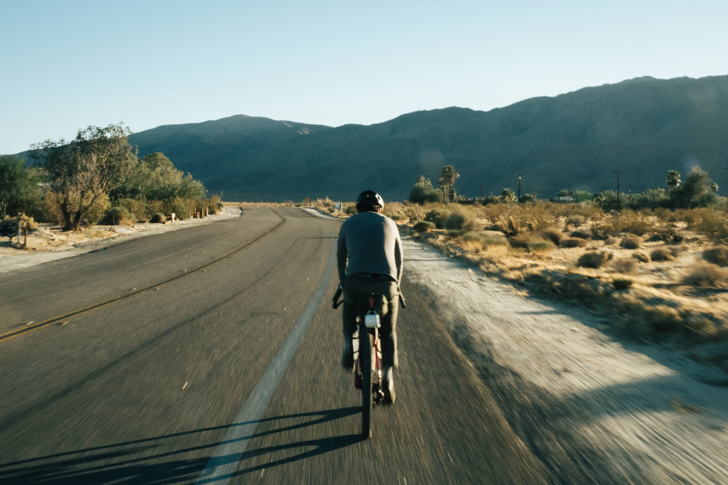 A person riding a bicycle on a paved road through a desert landscape with mountains in the background during daytime.