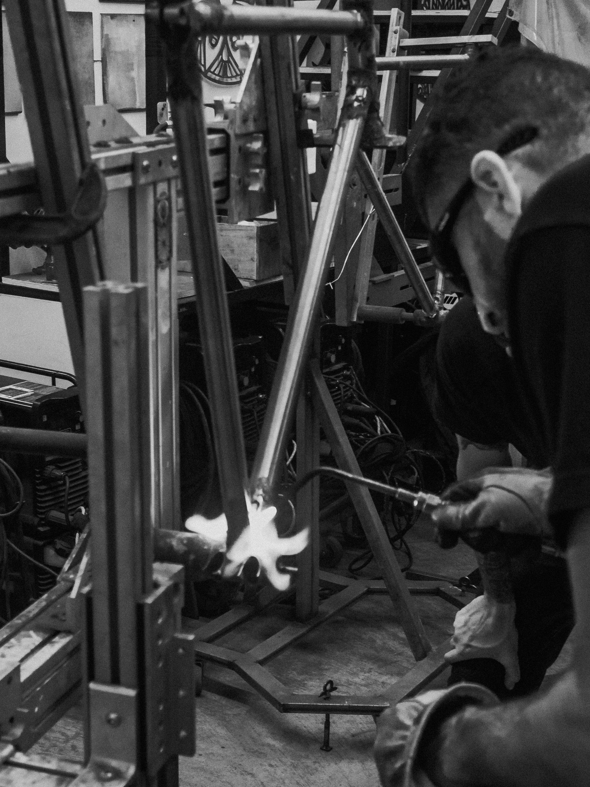 Person welding metal frame in workshop with tools and equipment around.