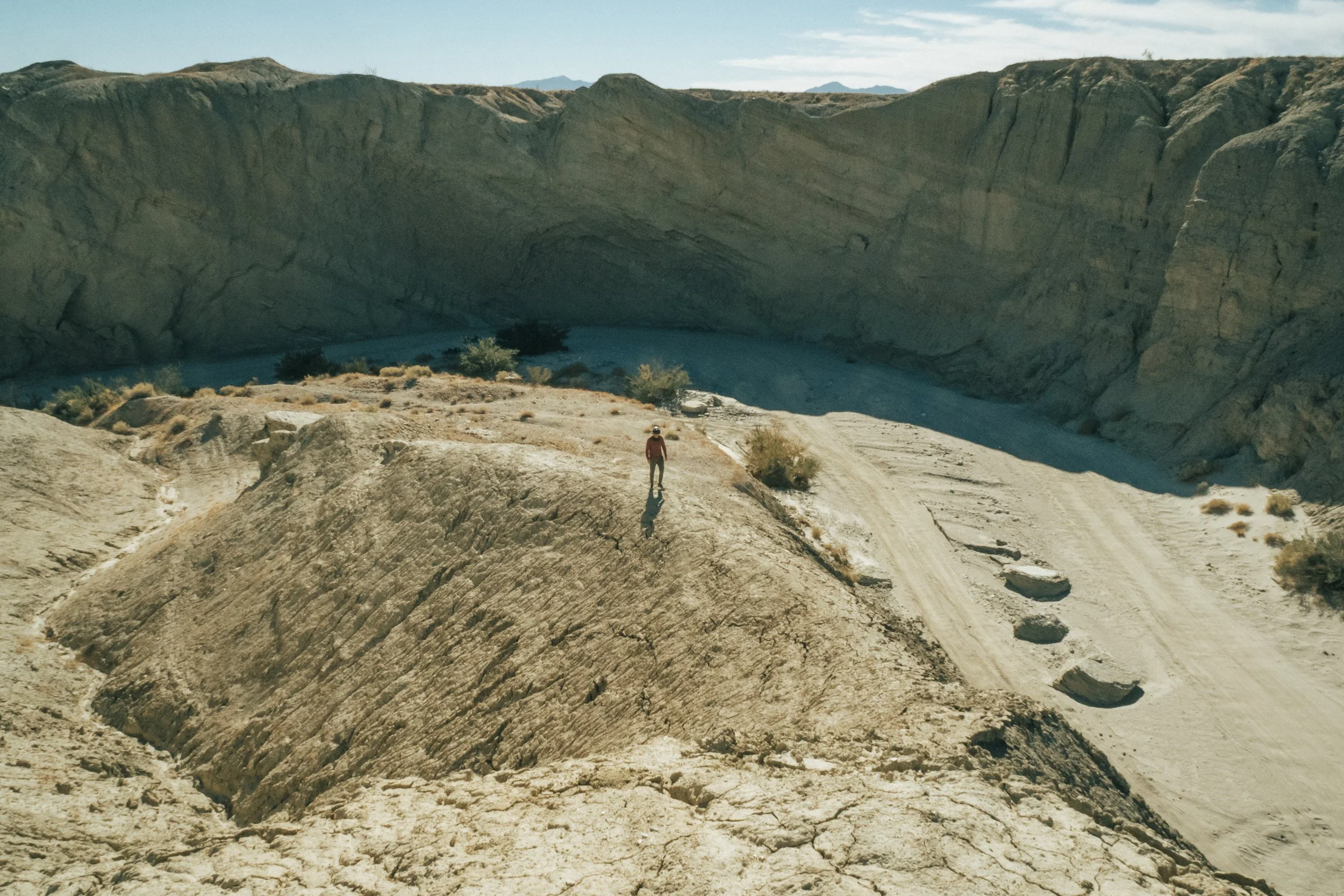 A person standing on a rocky hilltop in a desert landscape, with a canyon and sparse vegetation in the background.