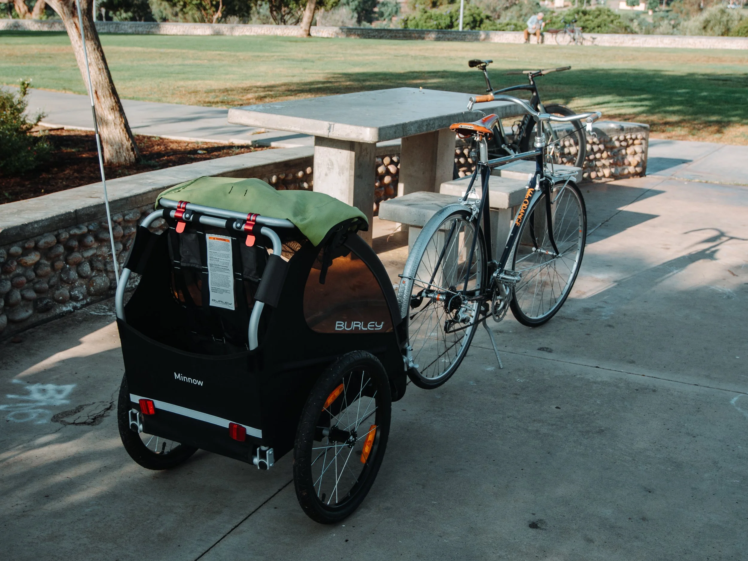 A bicycle with a child trailer attached, parked near a picnic table in a park.