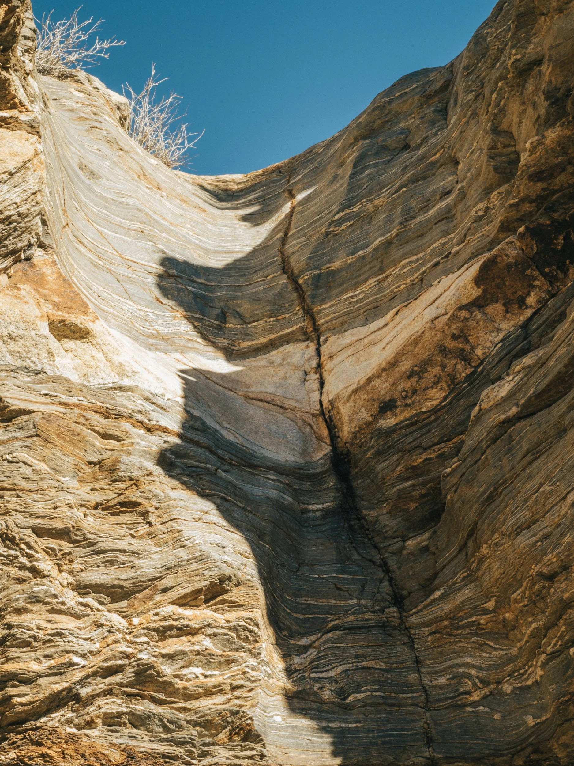 Close-up of layered rock formations with a prominent vertical crack, under a clear blue sky.