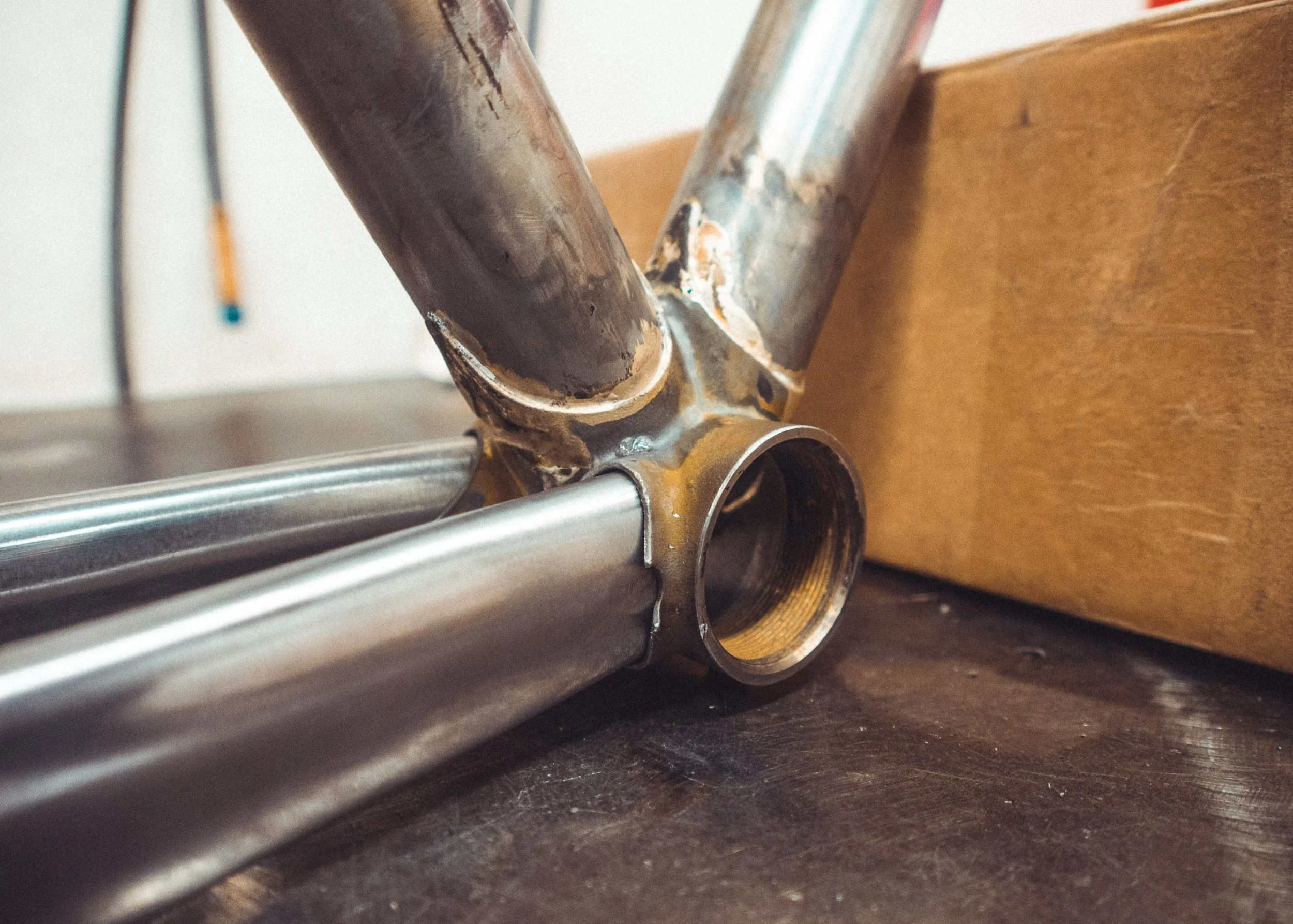 Close-up of the bottom bracket shell of a bicycle frame with part of the down tube and seat tube visible, showing signs of rust and wear.