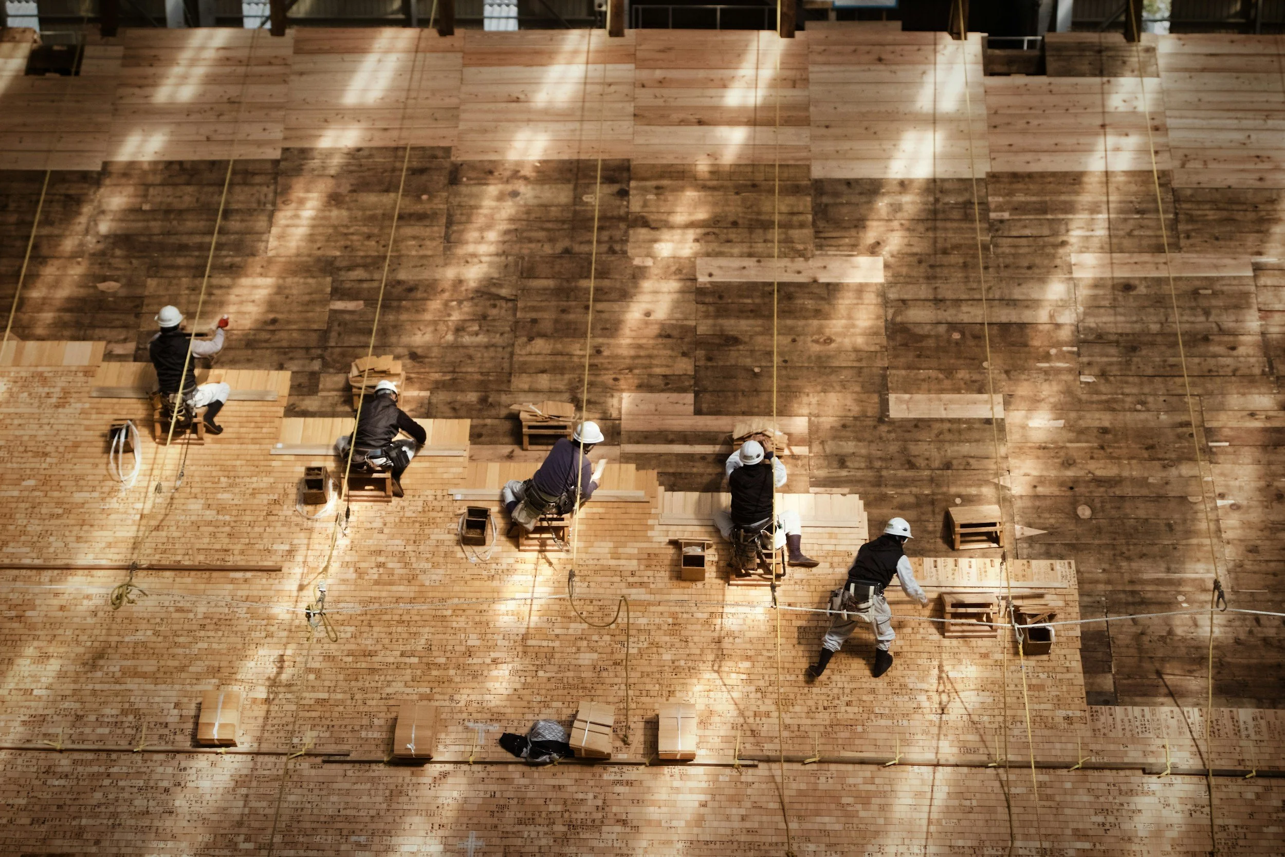 Construction workers installing wooden flooring in a large building, seen from above.